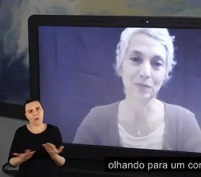 Cena de uma mulher branca na tela do notebook e à frente a intérprete de Libras